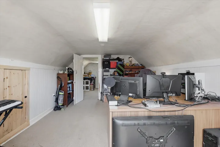 Attic room featuring a sloped ceiling, light-colored carpet flooring, white beadboard wainscoting, and a fluorescent overhead light fixture