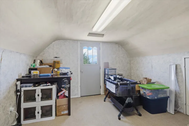 Attic space featuring sloped ceilings, carpet flooring, and a window for natural light