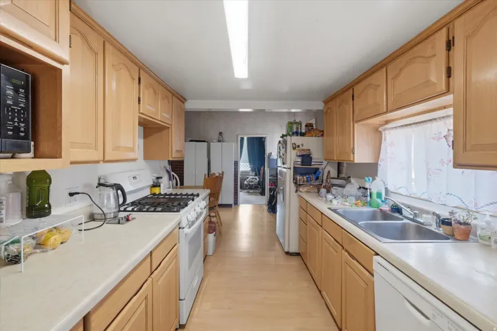 Galley kitchen featuring wood cabinetry, laminate countertops, wood-finish flooring, a double basin sink, and a four-burner gas range
