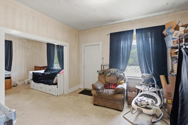 Carpeted room with a paneled door, window with dark curtains, and an open doorway leading to an additional space with a window