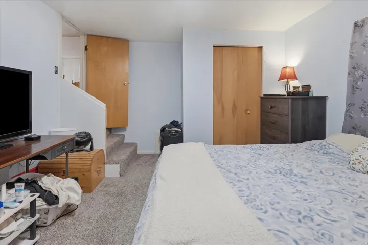 Carpeted room featuring a built-in closet with bi-fold doors, light blue painted walls, and a staircase with a wooden handrail