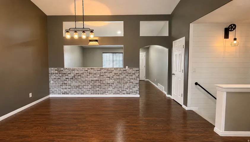 Rich wood-finish flooring, accent brick wall, recessed wall shelving, arched doorway, and a contemporary light fixture
