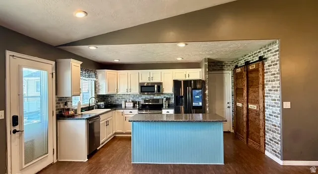 Kitchen featuring white cabinetry, dark countertops, a blue-painted island with beadboard paneling, stainless steel appliances, and wood-finish flooring