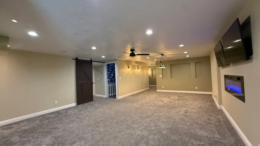 Spacious area featuring recessed lighting, a ceiling fan, a barn door, and a built-in electric fireplace