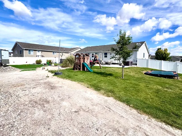 Expansive backyard featuring a green lawn, white privacy fencing, and a concrete patio