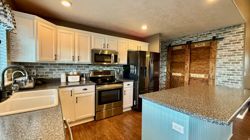 White cabinetry with black hardware, stainless steel appliances, brick-look backsplash, wood-finish flooring, and a kitchen island with a speckled countertop