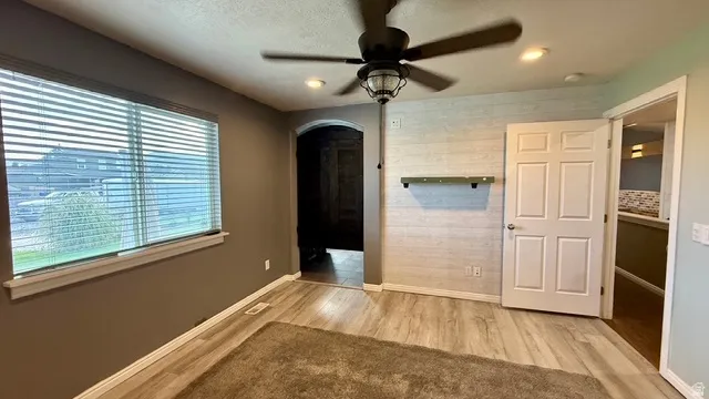 Recessed ceiling lighting, wood-finish flooring, ceiling fan with integrated light, and a window with blinds