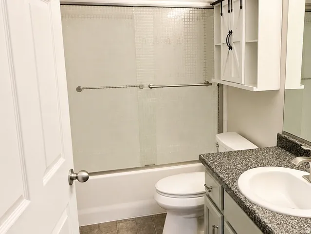 Shower-tub combination with sliding glass doors, vanity with integrated sink, patterned flooring, and wall-mounted storage cabinet