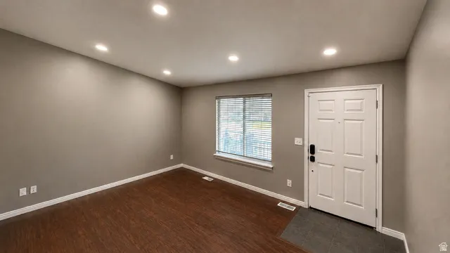 Recessed ceiling lighting, wood-finish flooring, neutral wall tones, white trim, and a paneled entry door