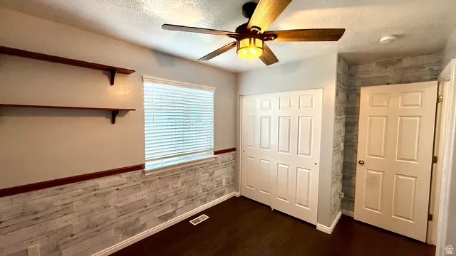 Wood-finish flooring, built-in shelving, paneled accent wall, window with blinds, and a ceiling fan with integrated lighting