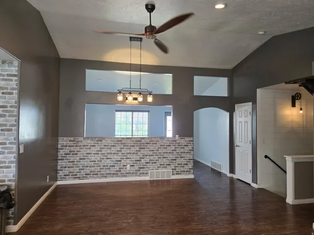 Vaulted ceilings, wood-finish flooring, accent brick wall, recessed lighting, and a modern ceiling fan with integrated lighting