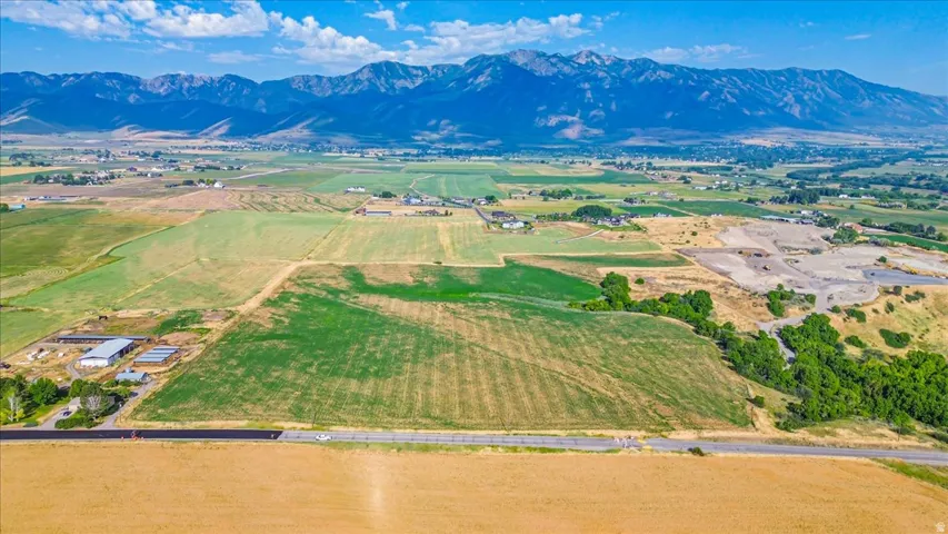 Expansive rural landscape featuring a paved road, agricultural fields, distant mountain range, and scattered structures