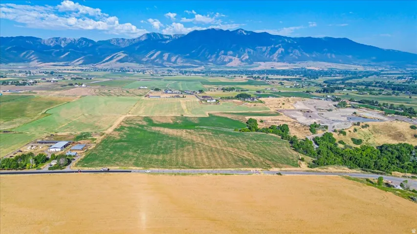 Expansive agricultural landscape featuring a flat, cleared field in the foreground, diverse vegetation across the midground, and distant mountains under a clear sky