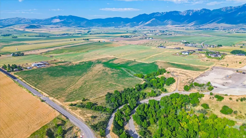 Expansive rural landscape featuring a paved road, agricultural fields, distant mountains, and scattered trees