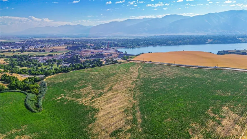 Expansive acreage featuring green and golden fields, a roadway, and distant water