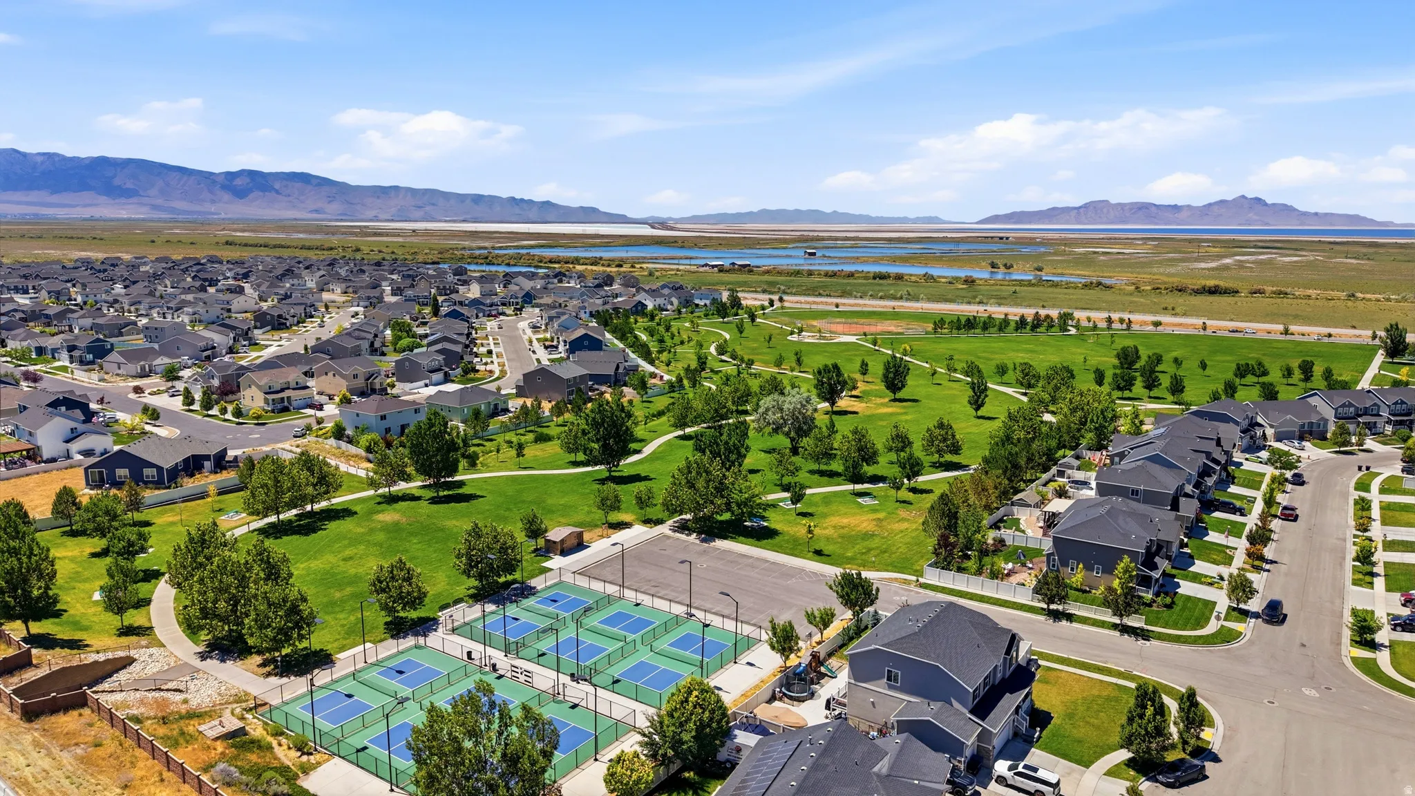 Expansive park area featuring multiple pickleball courts, manicured green space, and walking paths surrounded by a residential neighborhood