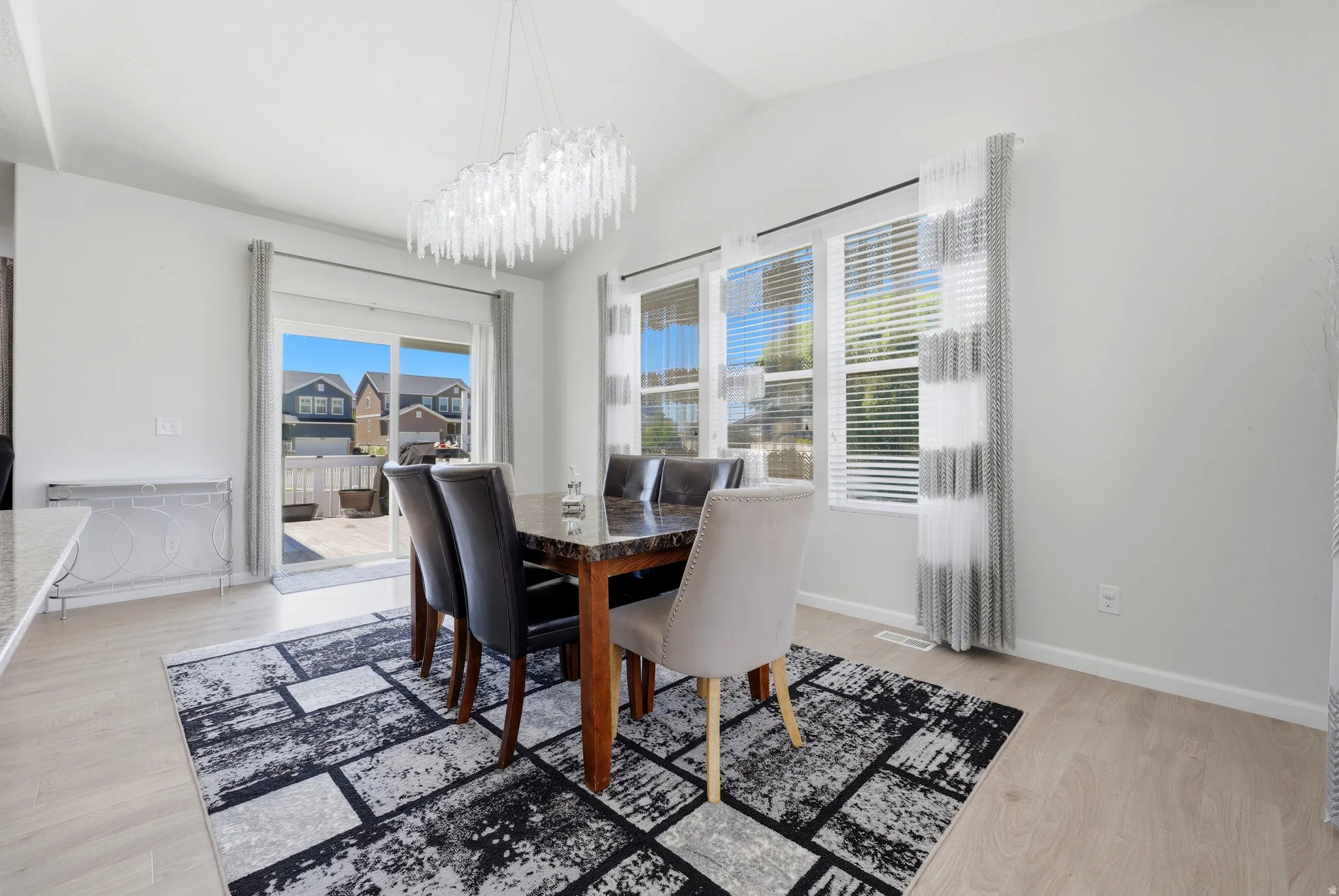 Dining area featuring vaulted ceilings, wood-finish flooring, and a sliding glass door providing outdoor access to the deck