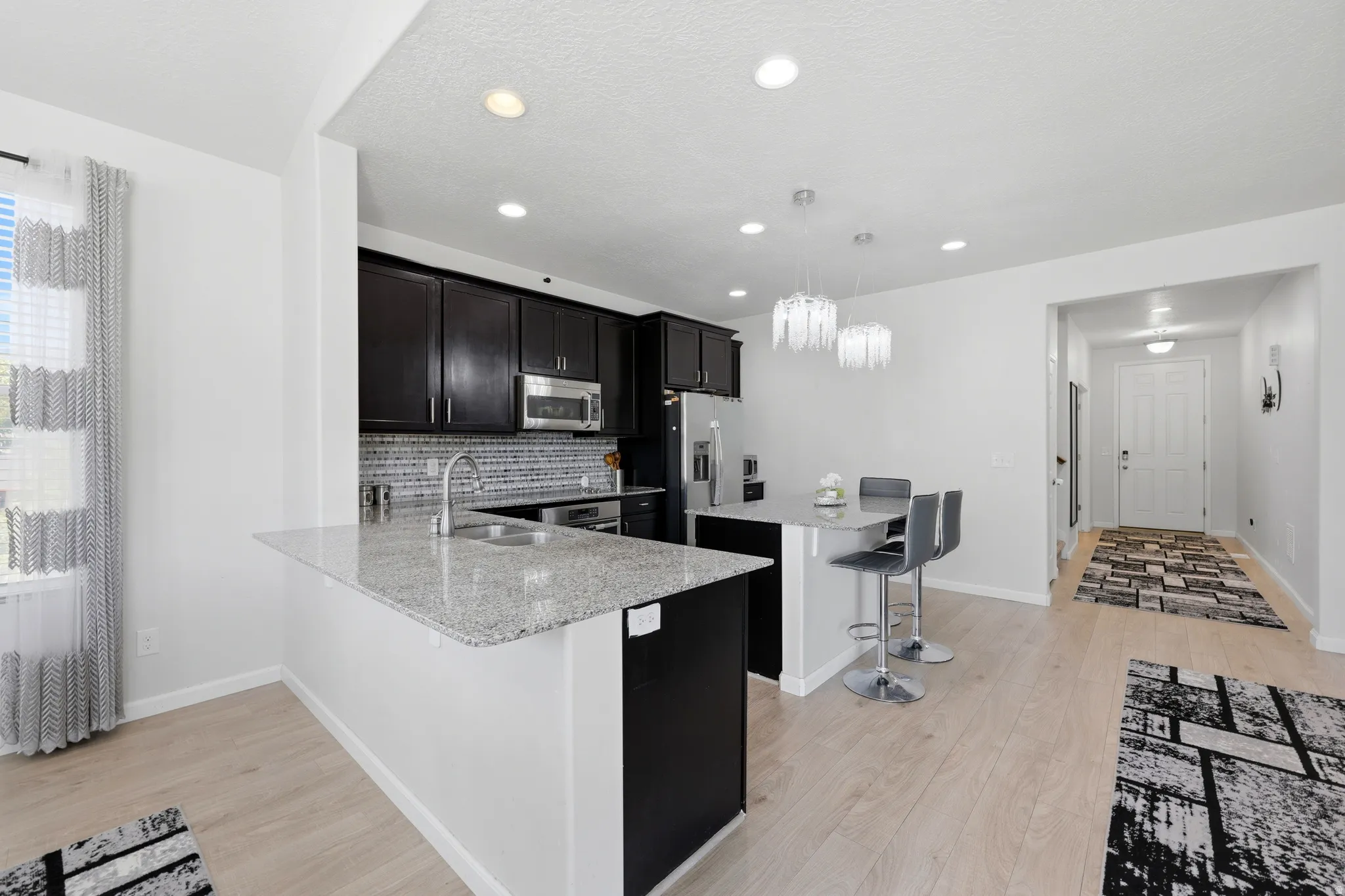 Modern kitchen featuring dark wood cabinetry, stainless steel appliances, speckled stone countertops, and a tiled backsplash