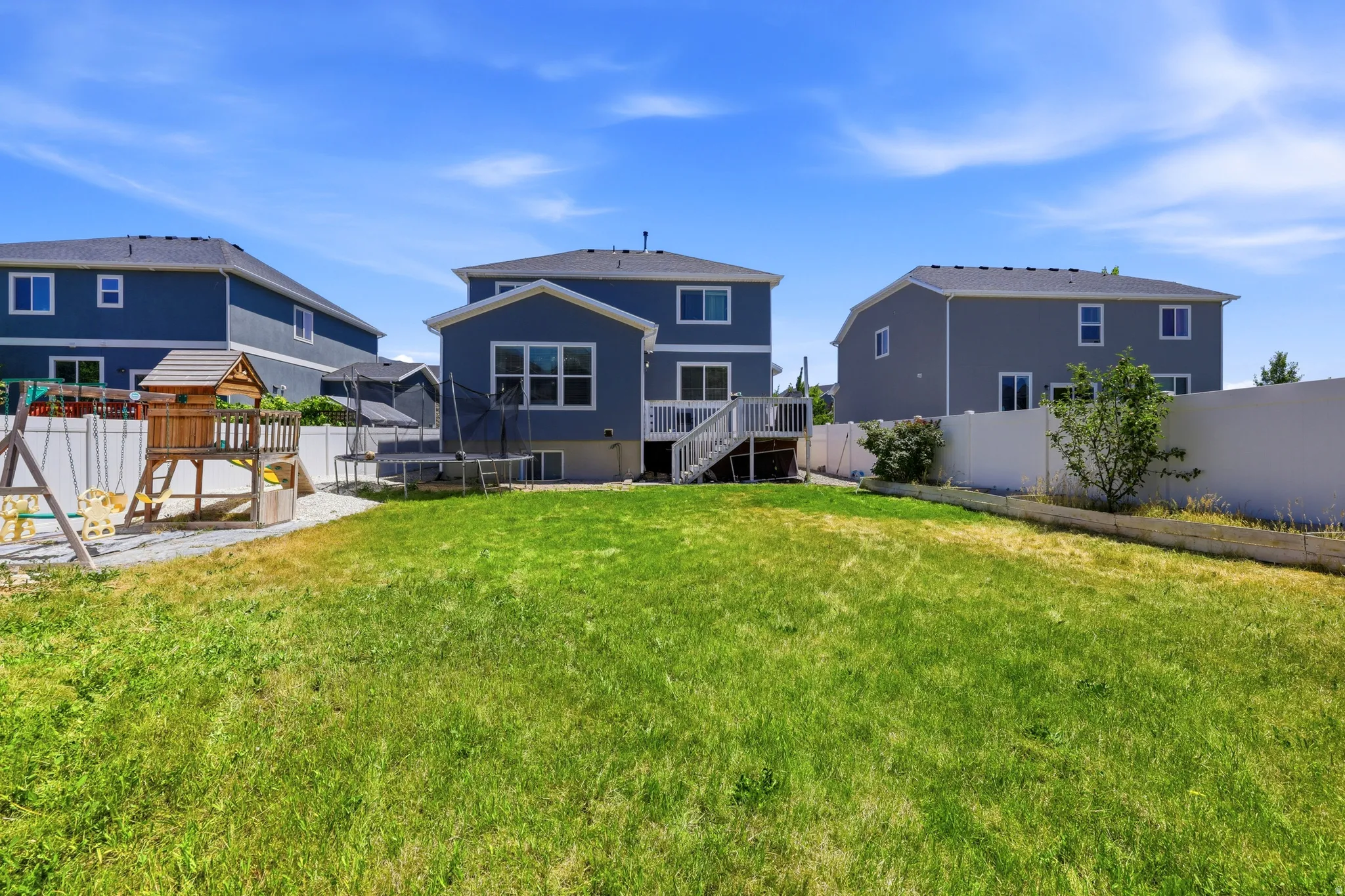 Expansive backyard with a green lawn and white privacy fencing