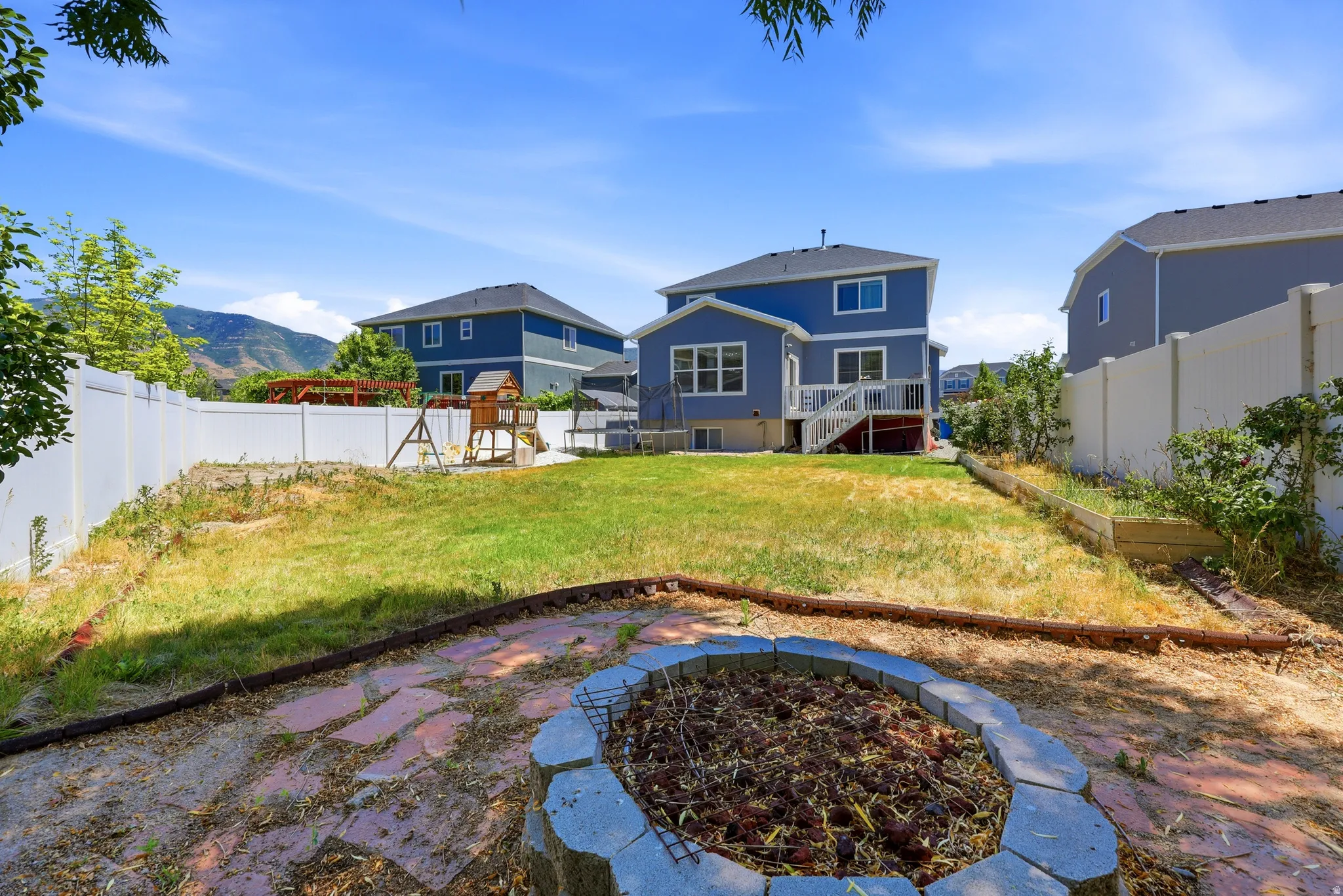 Backyard featuring a natural gas stone fire pit area, extensive lawn space, and a composite deck with stairs