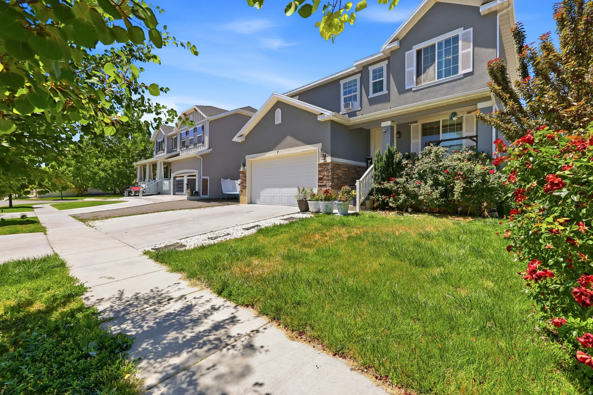 Gray stucco exterior featuring a covered porch with white railings, a front-facing garage, and white window shutters
