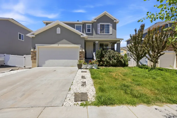 Two-story stucco residence with a two-car garage, concrete driveway, and white picket fencing