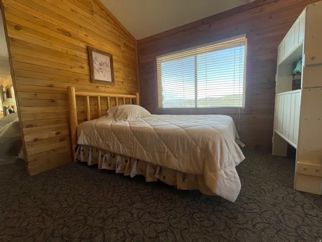 Wood-paneled room featuring a window with horizontal blinds, a wood-frame bed, and patterned carpet