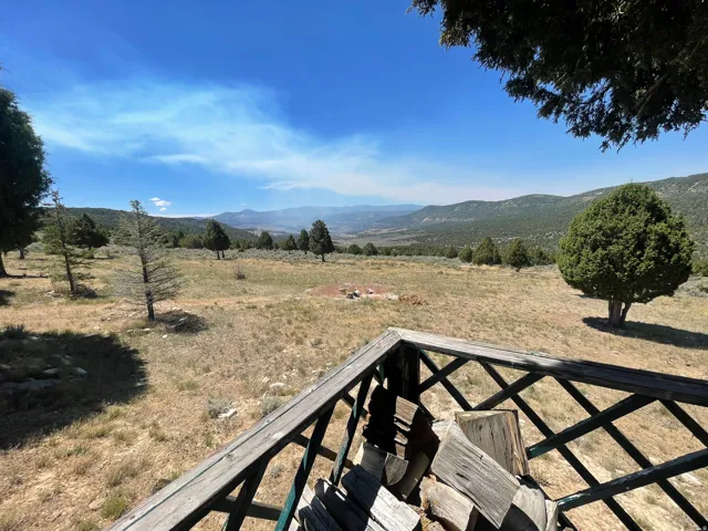 Expansive outdoor space featuring a wooden deck with lattice railing, mature trees, and distant mountain scenery