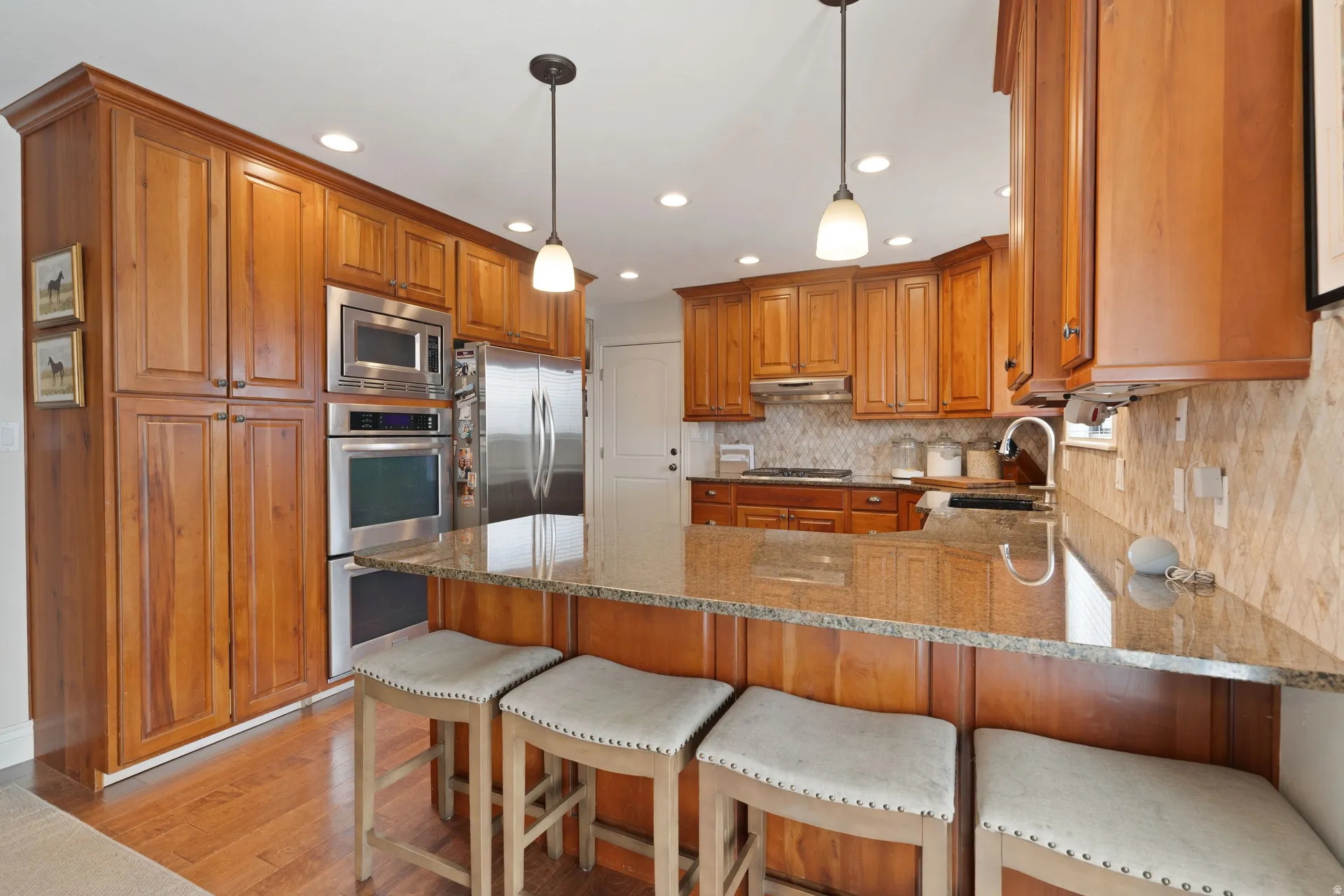 Kitchen featuring wood cabinetry, stainless steel appliances including a built-in microwave and double oven, light-toned backsplash, granite countertops, and recessed lighting
