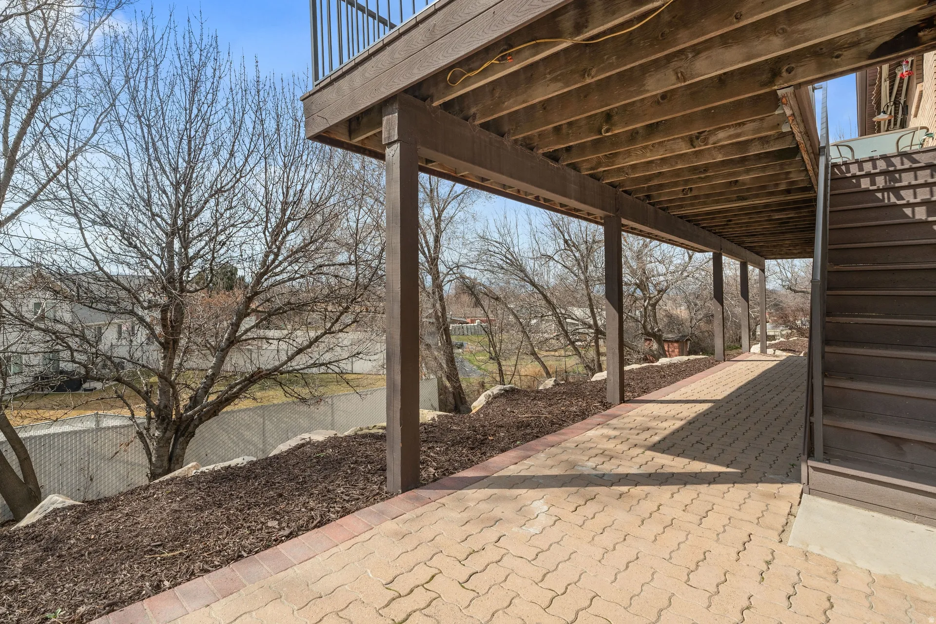 Covered patio featuring a paver walkway, wood support beams, and a wood staircase
