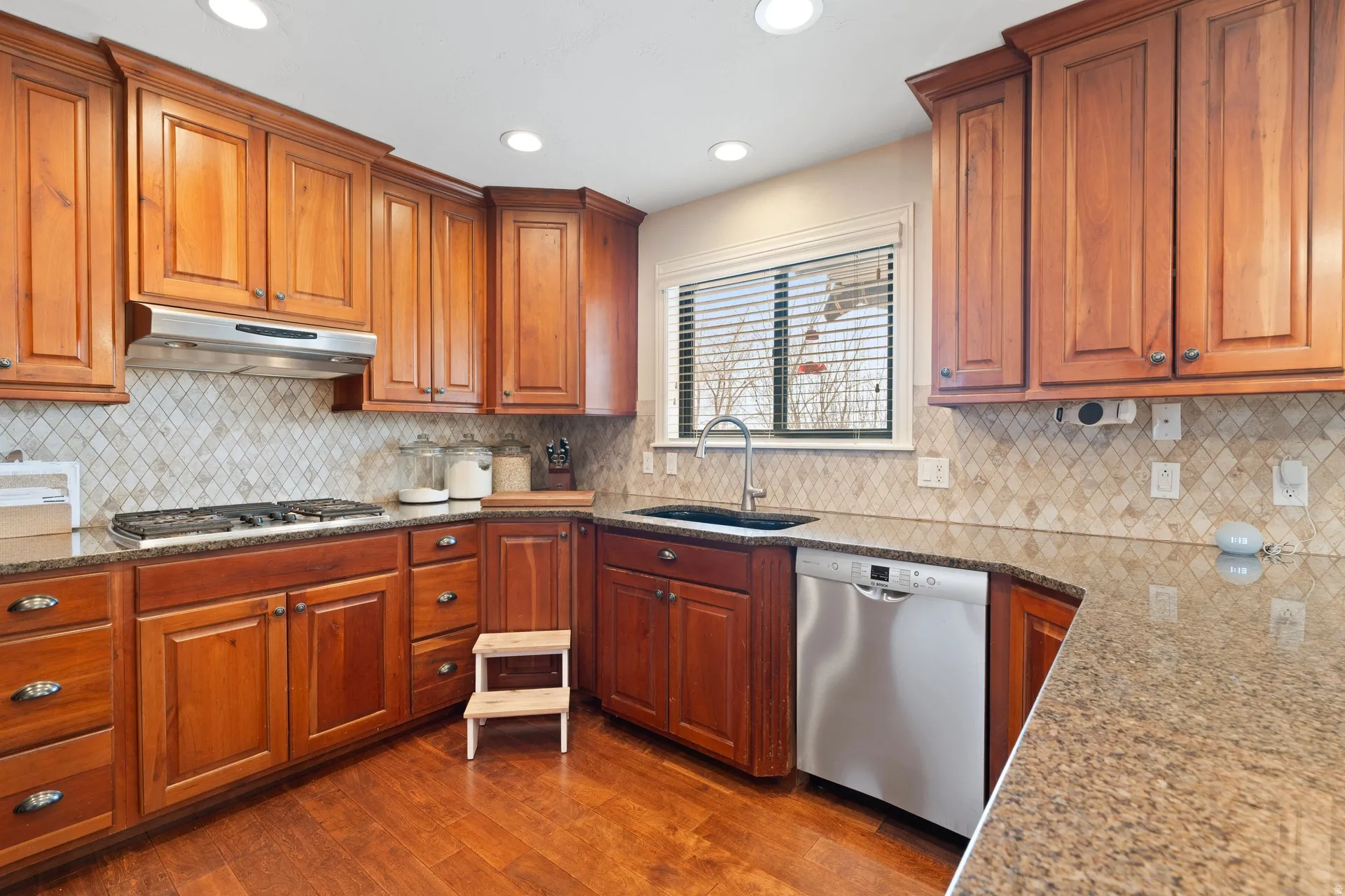 Kitchen featuring wood cabinetry, stainless steel appliances, speckled countertops, and a diagonal tile backsplash