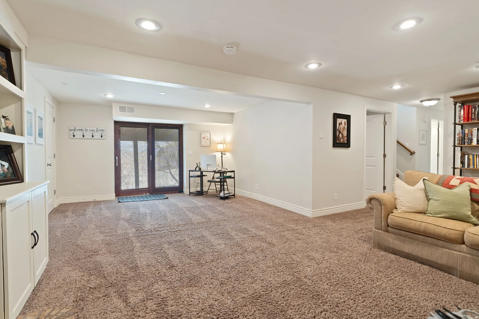 Spacious room featuring plush carpeting, recessed lighting, and a built-in shelving unit with cabinet storage