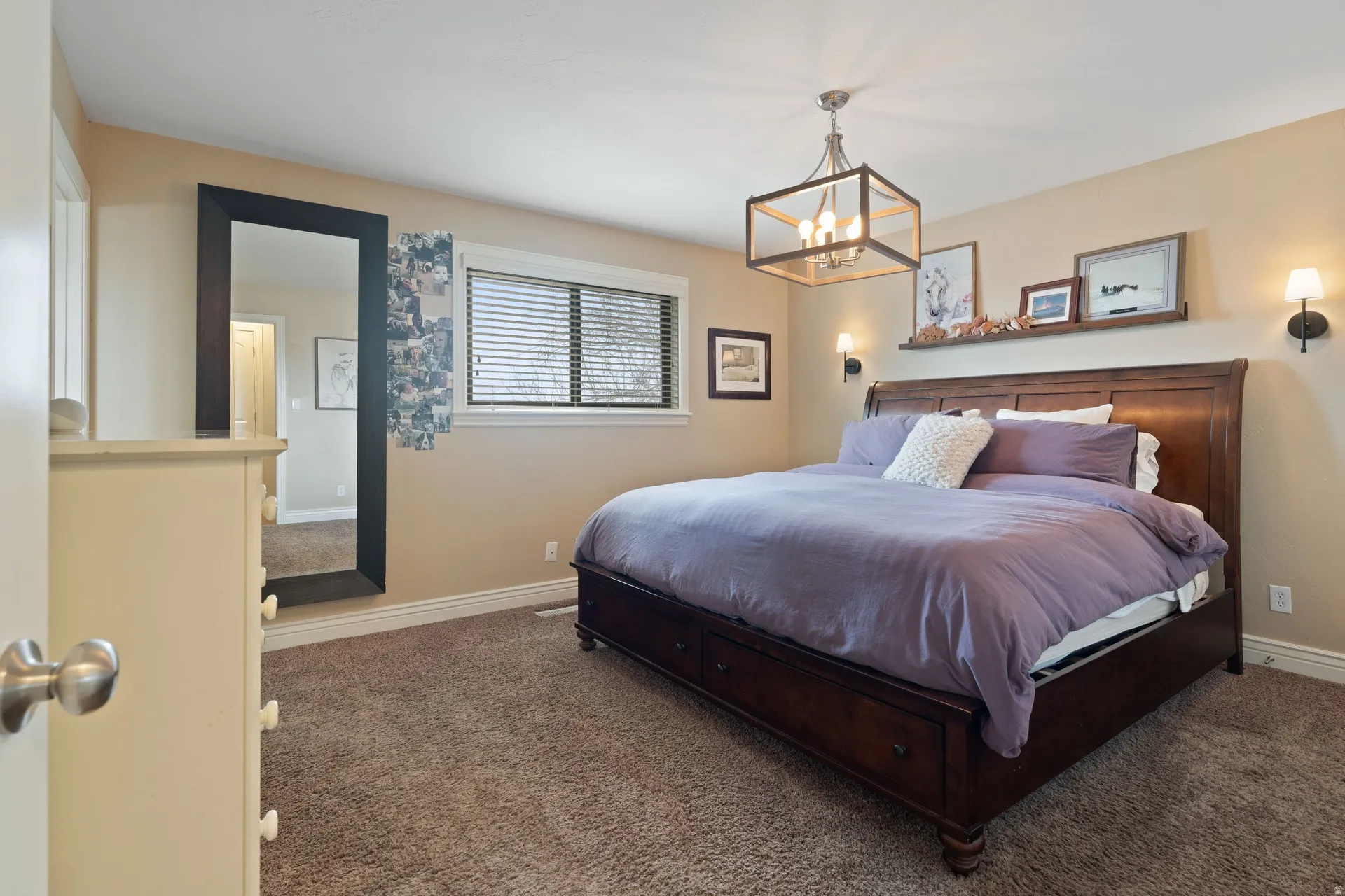 Carpeted bedroom featuring a window with horizontal blinds, a ceiling-mounted light fixture, and two wall sconces
