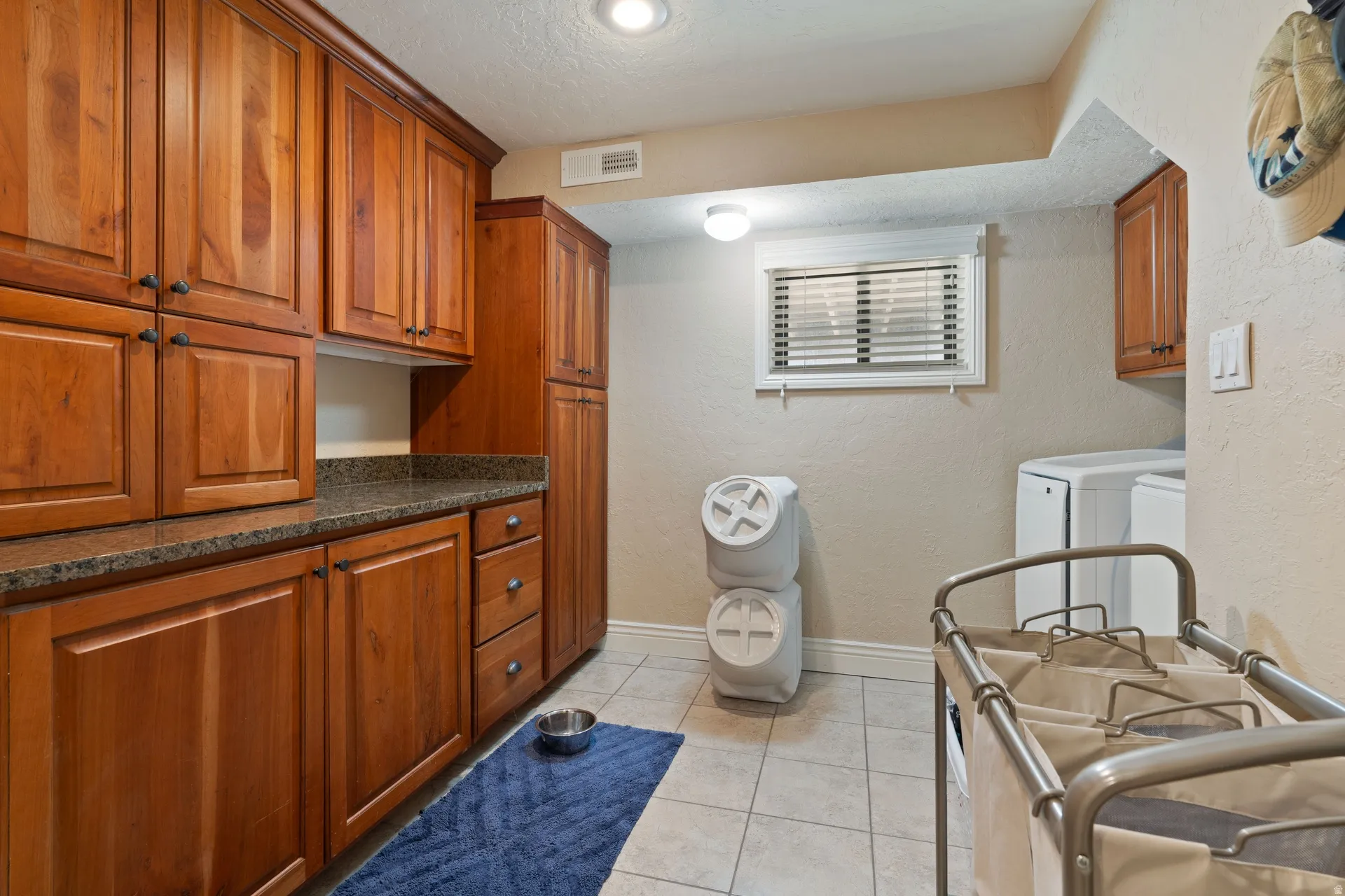 Laundry area featuring extensive wood-finish cabinetry, a stone-finish countertop, and tile flooring