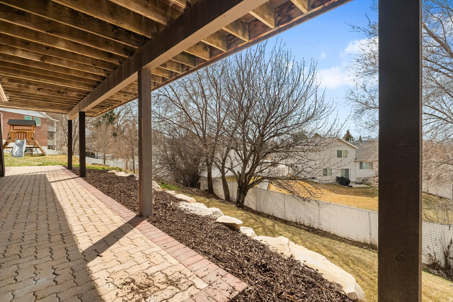 Covered patio featuring an interlocking paver surface, timber support beams, and a natural wood ceiling