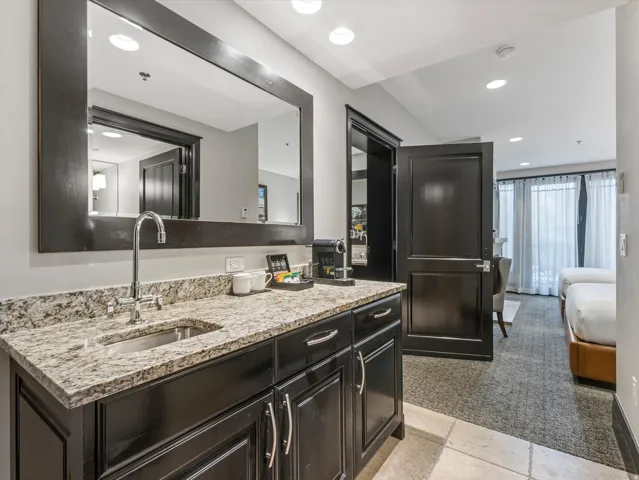 Wet bar featuring a dark wood base cabinet with silver hardware, speckled granite-style countertop, and an undermount stainless steel sink with a chrome faucet