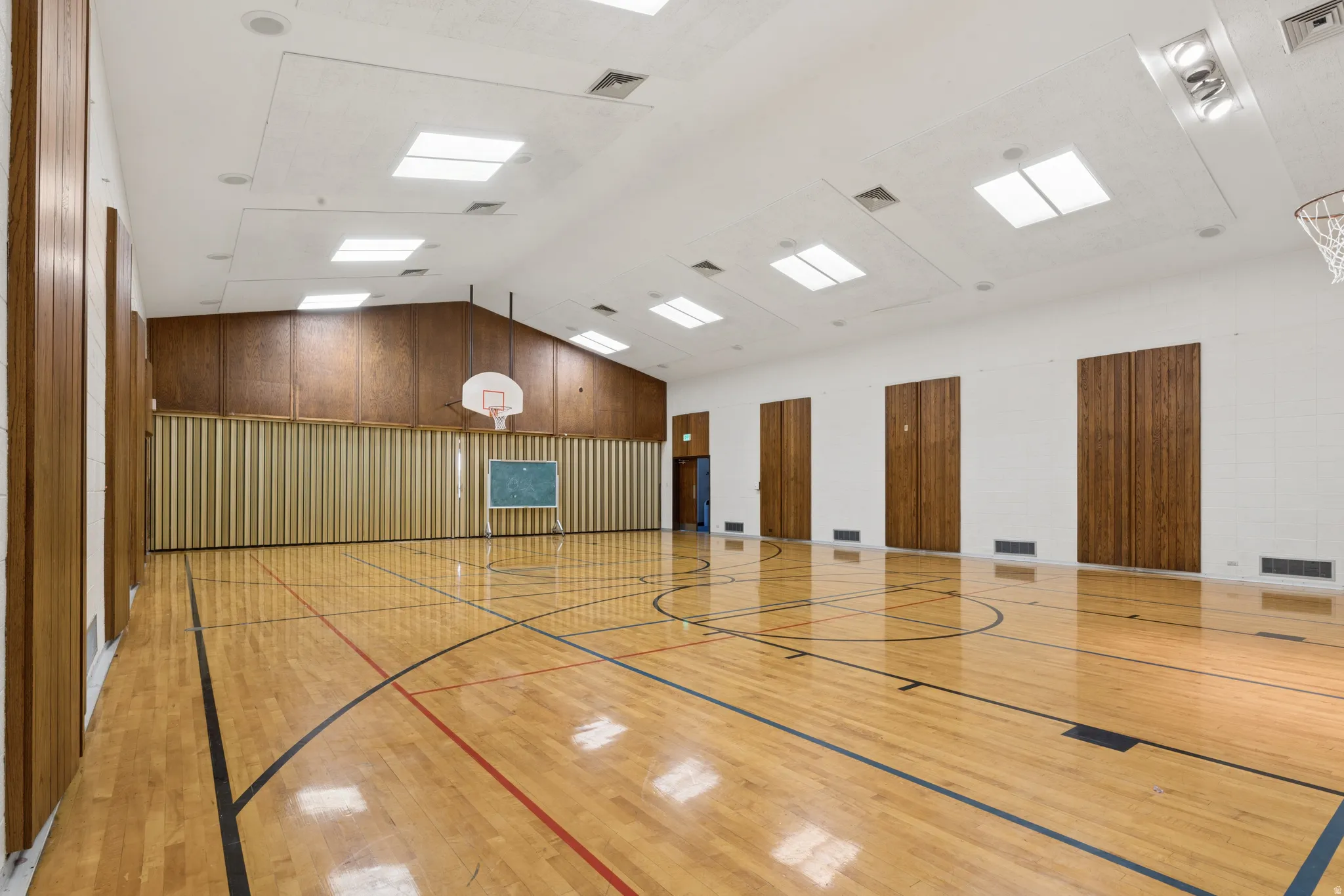 Spacious indoor court featuring polished wood flooring with court markings, a high vaulted ceiling, multiple skylights, and integrated lighting