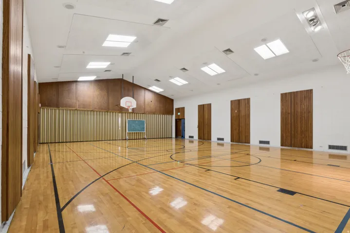 Spacious indoor court featuring polished wood flooring with court markings, a high vaulted ceiling, multiple skylights, and integrated lighting