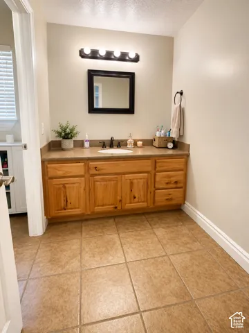 Bathroom vanity featuring light wood cabinetry, a beige countertop, an undermount sink, and a black framed mirror
