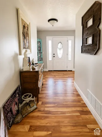 Entryway featuring wood-finish flooring, a white paneled door with an oval leaded glass insert, and two vertical sidelight windows