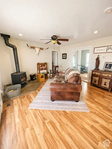 Open living area featuring wood-finish flooring, a ceiling fan, recessed lighting, a built-in wood-burning stove with stone hearth, and white French doors