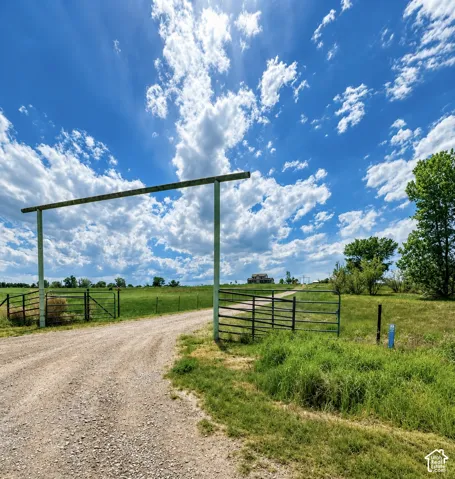 Gravel drive leading to a distant residence, framed by an overhead archway and metal fencing