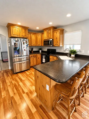 Kitchen featuring wood-finish flooring, natural wood cabinetry, dark countertops, a stainless steel refrigerator, and recessed lighting