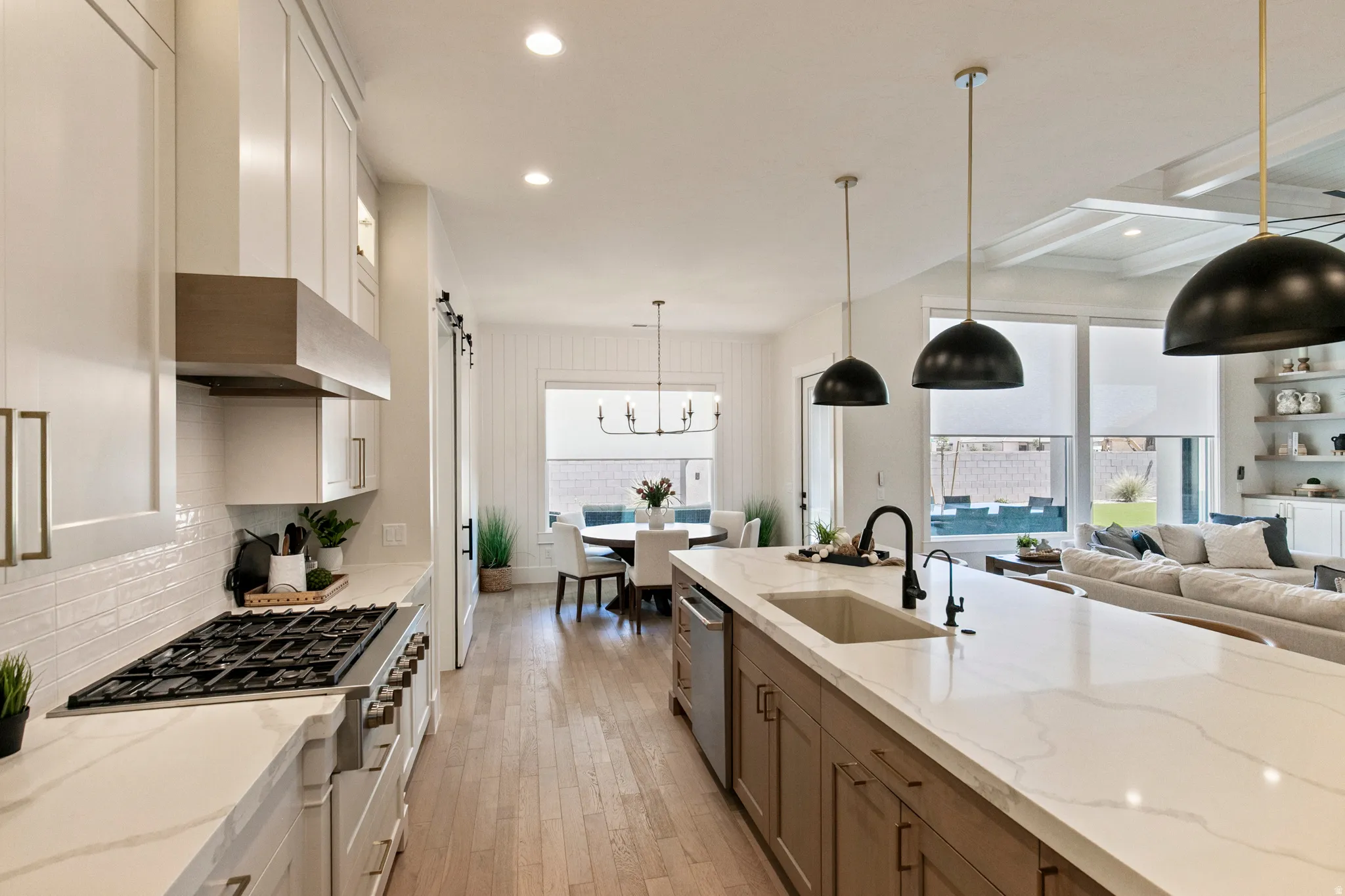 Expansive kitchen featuring a large island with sink, gas range with hood, white subway tile backsplash, and light wood-finish flooring