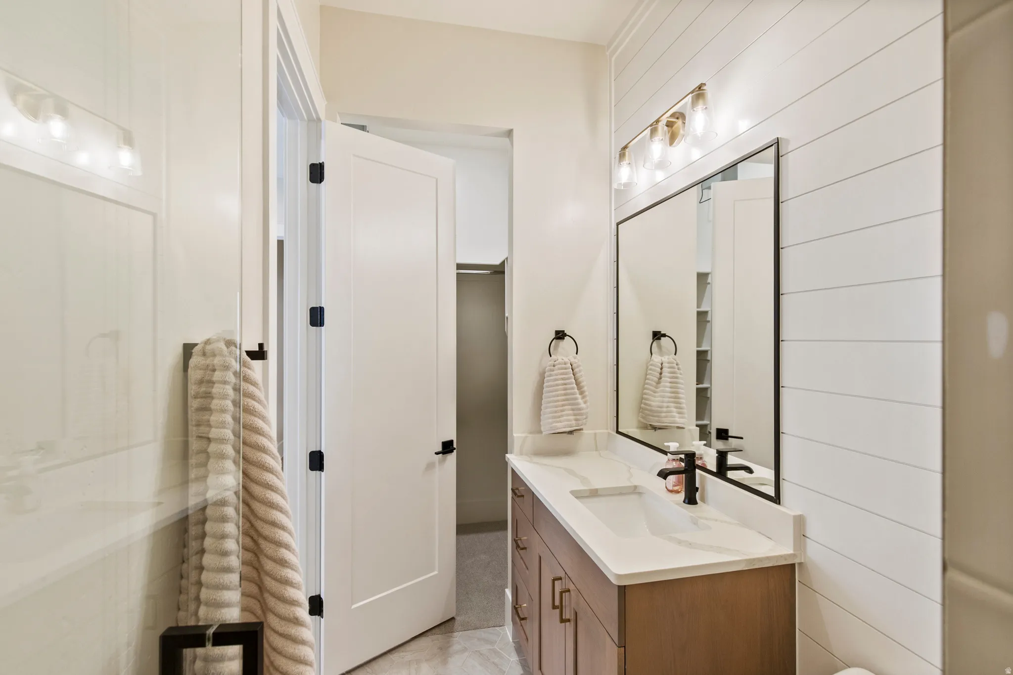 Bathroom vanity featuring a quartz countertop, integrated sink, and wood-finish cabinetry with matte black hardware