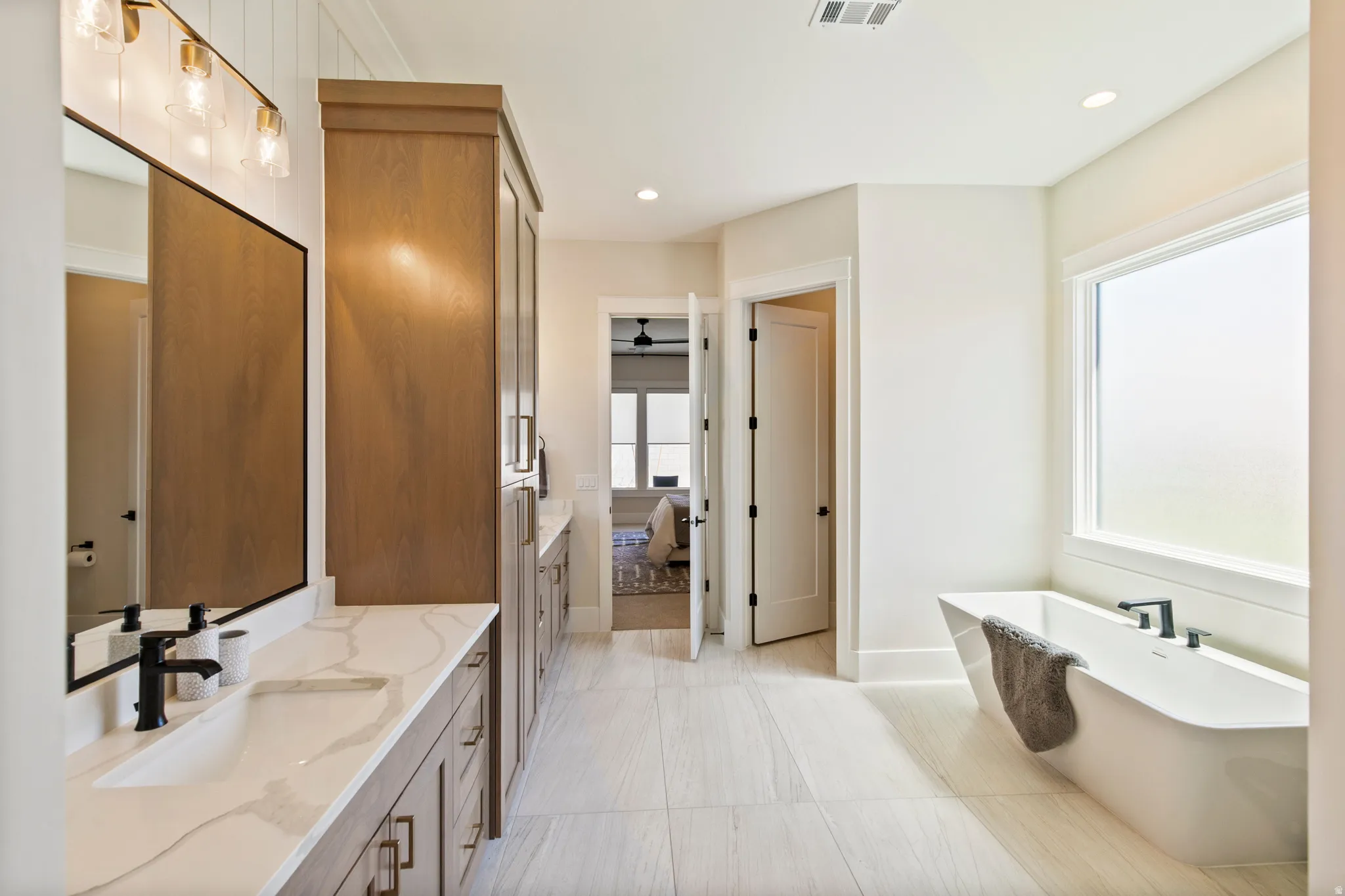 Spacious bathroom featuring a freestanding tub, expansive vanity with dual sinks, and wood-finish cabinetry