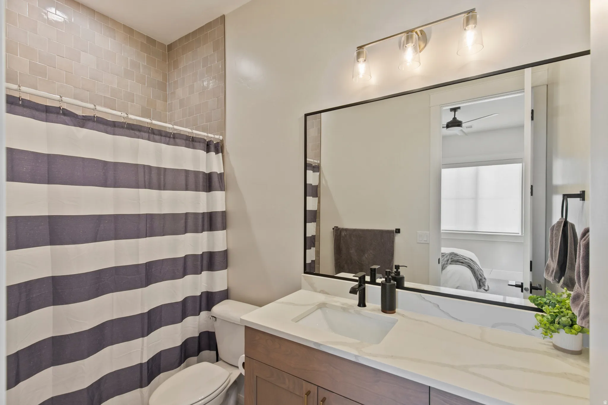 Bathroom featuring a wood-finish vanity with a white countertop and integrated sink, matte black faucet, and a large mirror with a three-bulb vanity light