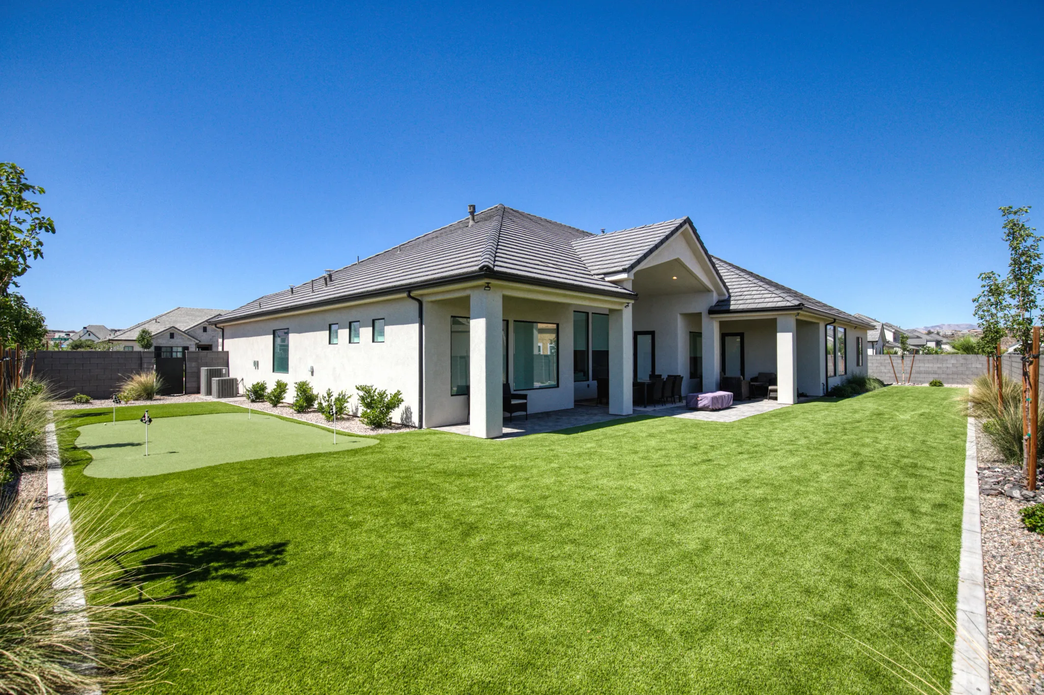 Rear exterior featuring a covered patio, extensive green lawn, and a putting green