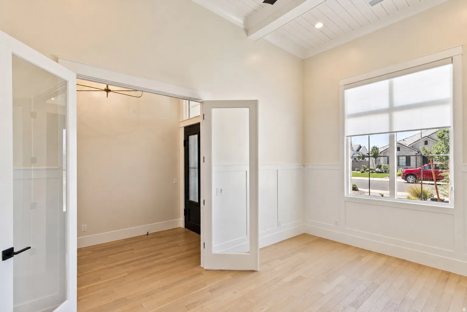 Bright room featuring wood-finish flooring, wainscoting, a large window with roller shades, and a coffered ceiling with recessed lighting