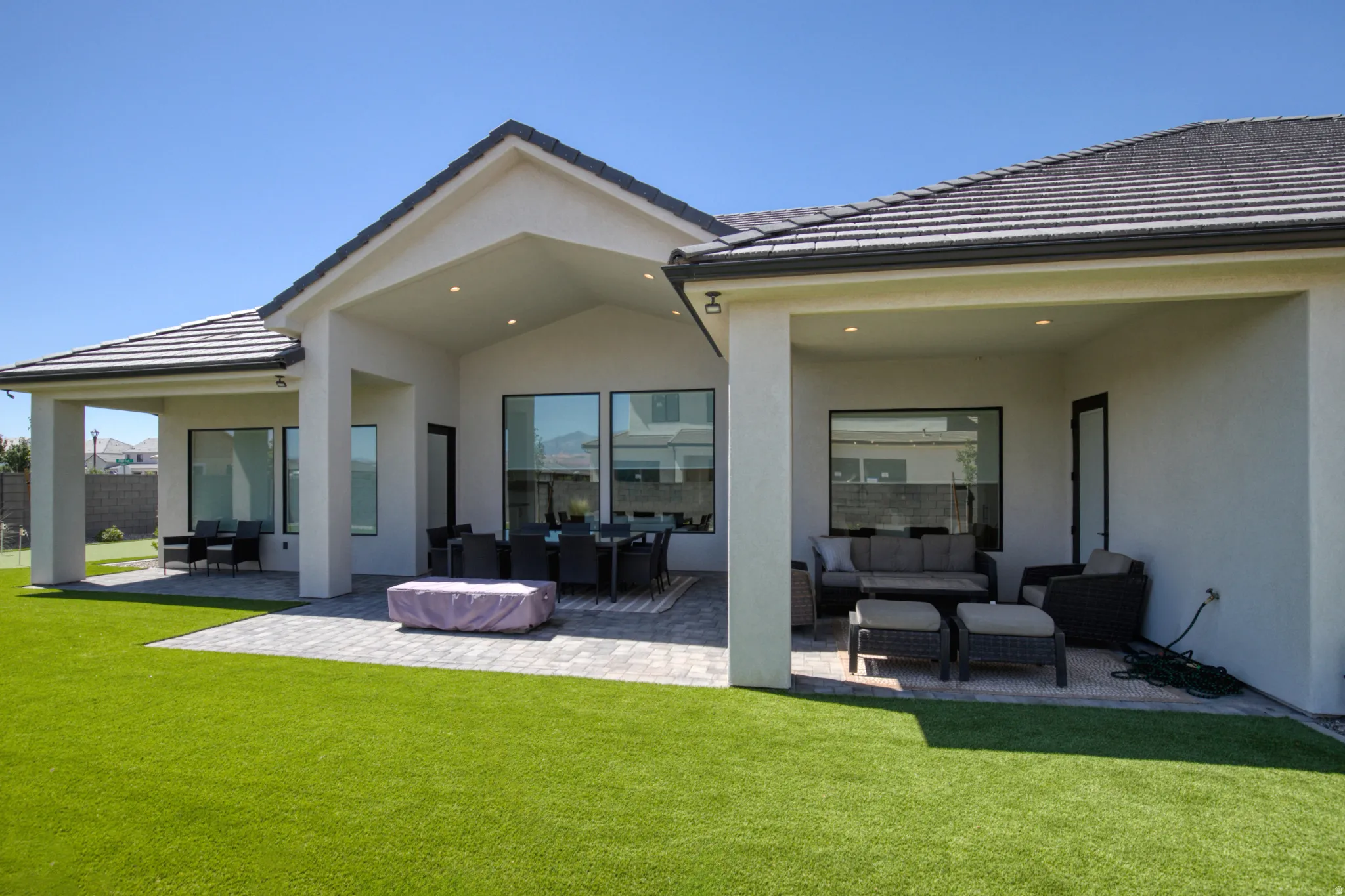 Expansive backyard featuring a large artificial turf lawn and a paver patio with multiple covered outdoor living areas